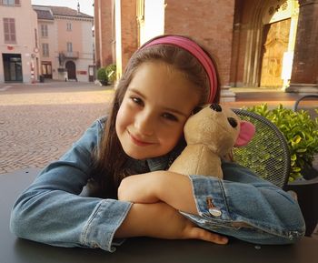 Portrait of smiling innocent girl with stuffed toy sitting on chair