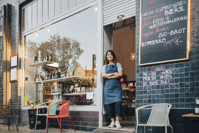 Full length portrait of female owner standing at entrance of deli