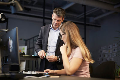 Creative businesswoman looking at male bank manager holding solar toy car in creative office