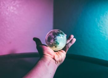 Cropped hand holding crystal ball against wall