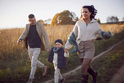 Family of three people runs along the road to the field in autumn at sunset