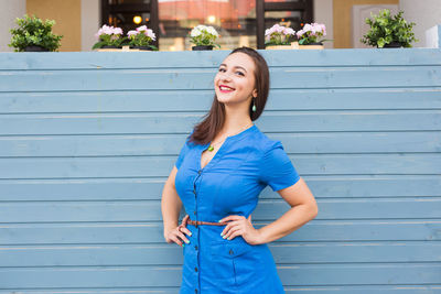 Portrait of smiling young woman standing against blue wall