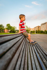 Side view of boy sitting on bench at park