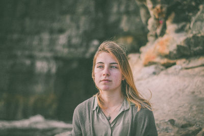 Thoughtful woman looking away against rock formation