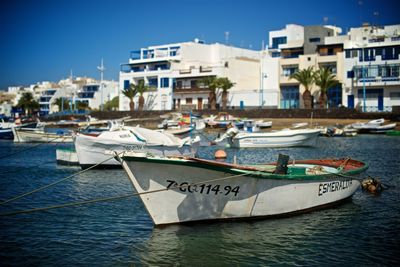 Sailboats moored on sea by buildings in city against sky