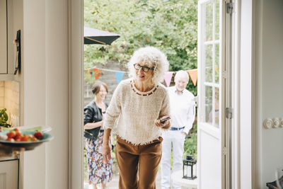 Smiling woman with curly white hair walking through doorway against friends