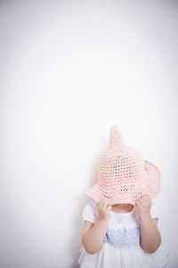 Rear view of girl wearing hat standing against wall