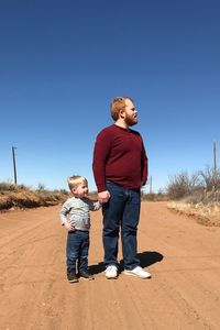 Full length of father and son standing against clear blue sky