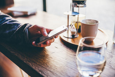 Cropped image of person using mobile phone by tea cup on table