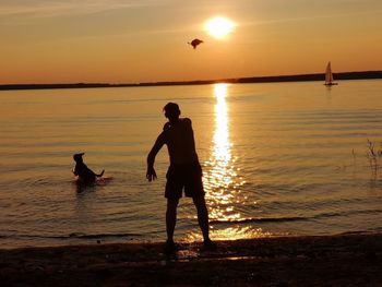 Silhouette people on sea against sky during sunset