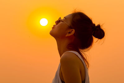 Woman with closed eyes against clear orange sky during sunset