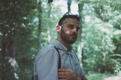 Young man looking away while standing in forest