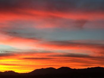 Scenic view of dramatic sky over silhouette mountains during sunset