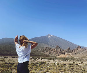 Rear view of woman standing on mountain against clear blue sky