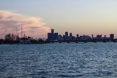 Sea by buildings against sky during sunset