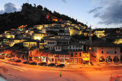 Road by illuminated buildings in city against sky at dusk