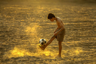 Side view of boy playing with ball at sunset