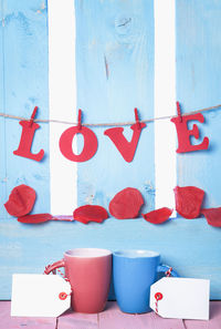 Close-up of love text hanging over petals and mugs