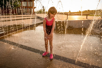 Joyful young girl in bathing suit plays at a splash pad at sunset