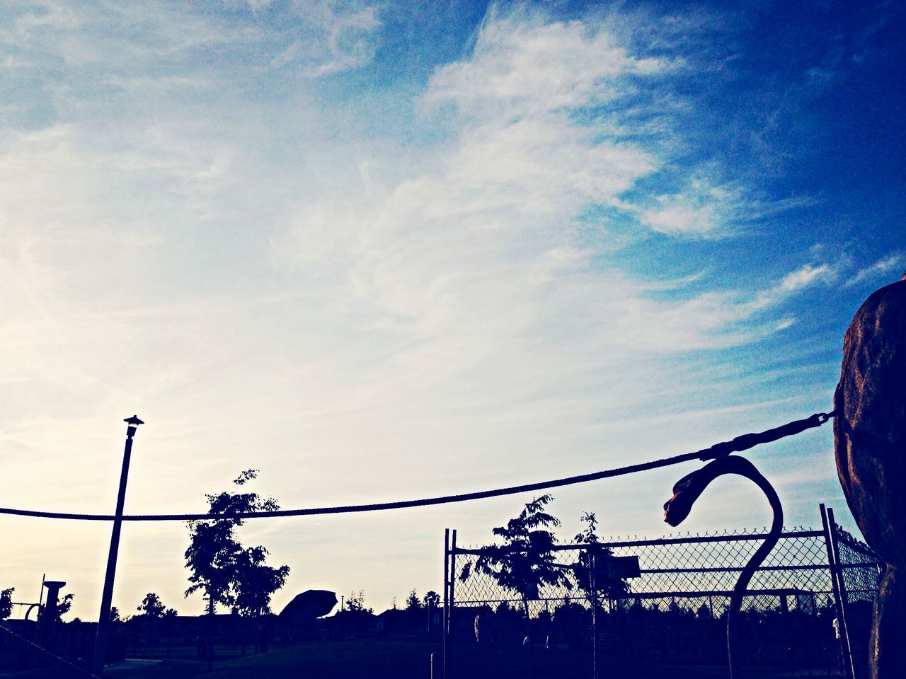 low angle view, silhouette, sky, street light, cloud - sky, tree, blue, cloud, power line, nature, connection, outdoors, lighting equipment, cable, dusk, high section, beauty in nature, railing, cloudy, no people