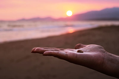 Close-up of hand on beach against sky during sunset