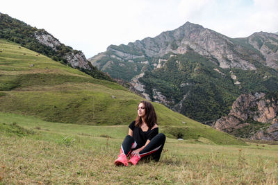 Young woman sitting on field against mountains