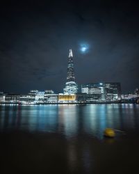 Illuminated shard in city by thames river against sky at night