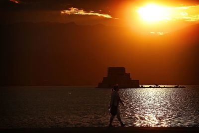 Silhouette man standing by sea against sky during sunset