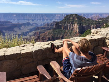 Rear view of man sitting on chair while looking at mountain range