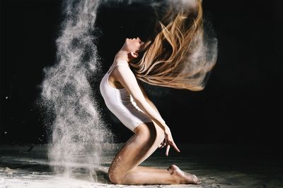 Young woman dancing with chalk powder against black background