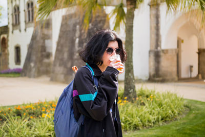 Young woman having drink while standing against plants