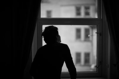 Silhouette woman looking through window