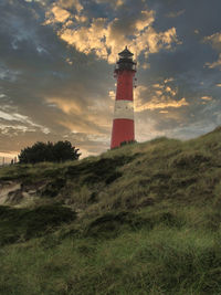 Lighthouse on field by building against sky