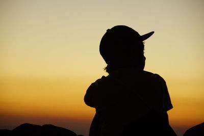 Silhouette boy standing against orange sky