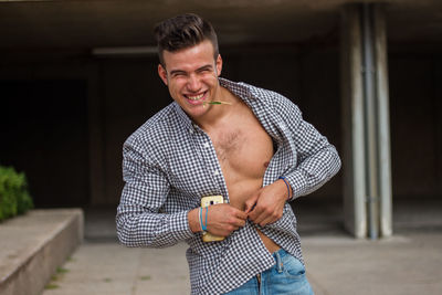 Cheerful young man opening his shirt while standing in city