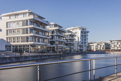 Buildings by river against clear sky in city