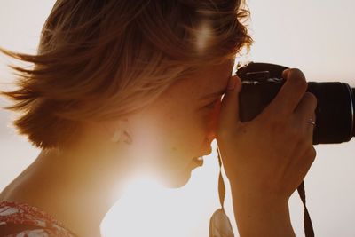 Close-up of woman photographing through camera against sky