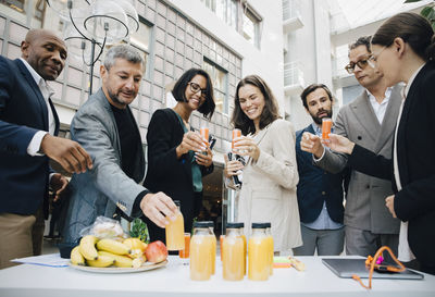 Smiling male and female business executives with juice outside office