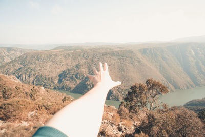 Person hand on mountain against sky