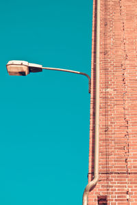 Low angle view of street light on brick wall against clear blue sky