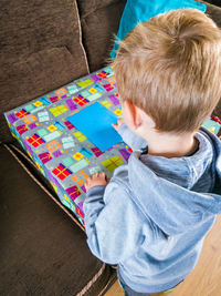 High angle view of boy with birthday present and envelope on sofa