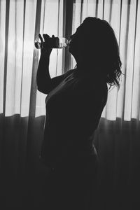 Side view of silhouette woman drinking water standing at home