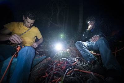 Two men sitting down organizing climbing gear in the dark after climb