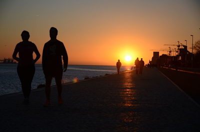 Rear view of silhouette man standing on beach against sky during sunset