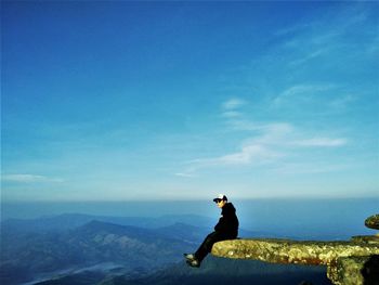 Man sitting on mountain against sky