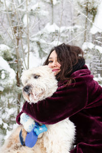 Young smiling woman is hugging her  dog on a background of winter coniferous forest.