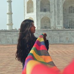 Woman holding colorful scarf in front of taj mahal