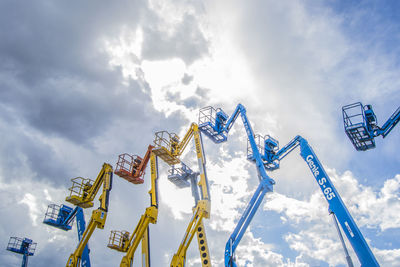 Low angle view of cherry pickers against cloudy sky