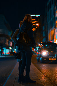 Rear view of man standing on city street at night