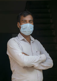 Portrait of young man wearing flu mask standing at home